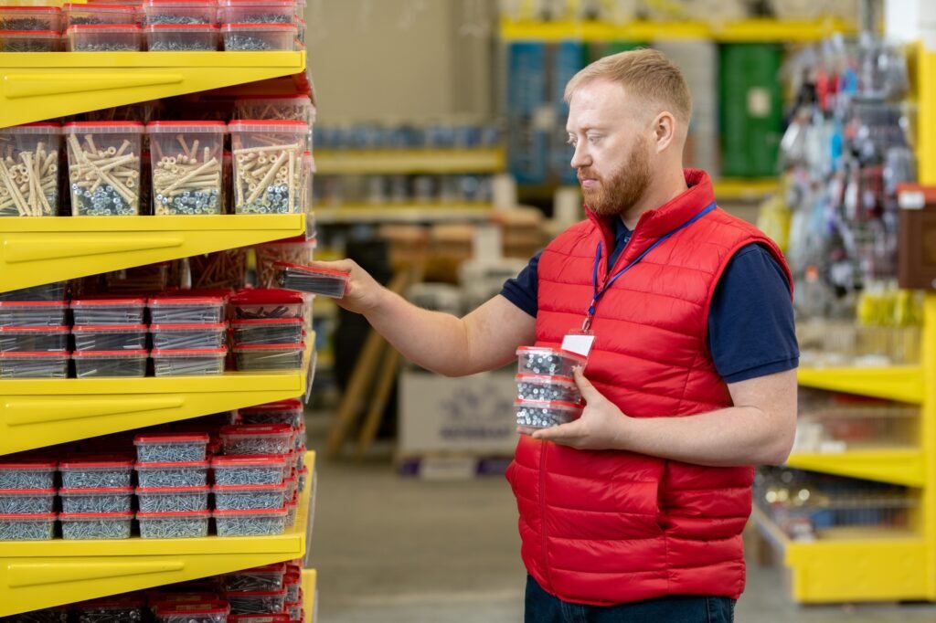 Bearded sales manager putting containers with nails on shelves