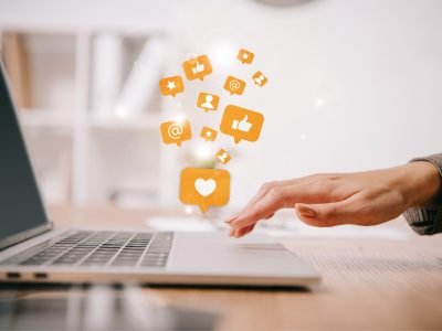 cropped view of businesswoman typing on laptop at workplace with multimedia icons